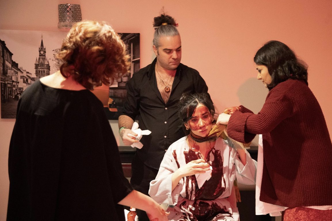 A woman covered in blood is tended to by three people, from Method to My Madness